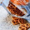 Crispy salted pretzels spilling from an open snack bag on a textured surface.